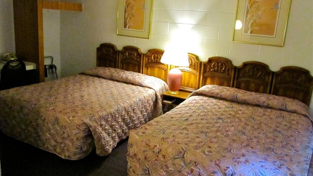 A hotel room with two double beds, a wooden headboard, a bedside table with a lamp, and two framed pictures on the wall. - Relax Inn (Cottage Grove)