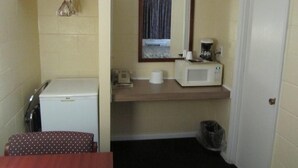 A compact kitchenette with a microwave, coffee maker, and a small refrigerator. A mirror hangs above the counter, and a trash can is visible. - Relax Inn (Cottage Grove)