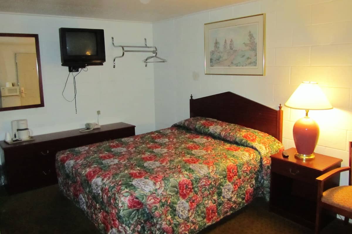 Una habitación de hotel con cama, mesita de noche, lámpara, televisor montado en la pared, un cuadro y un espejo.