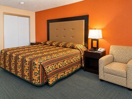 Quarto de hotel com uma cama grande, mesa de cabeceira com abajur e uma cadeira.