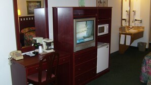 A compact hotel room with a wooden desk, a television, a microwave, a small refrigerator, a mirror, and a sink with a towel. - Shanico Inn (Lebanon)