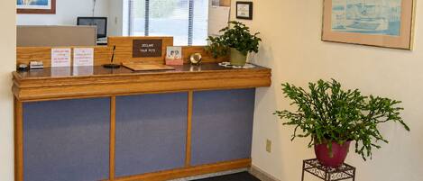 A reception desk with a check-out time sign, a clock, and a framed picture on the wall.
