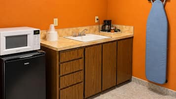A compact kitchen with a microwave, refrigerator, sink, and ironing board.