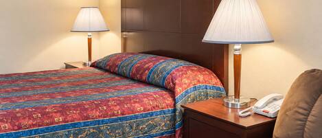 A hotel room with a bed, two bedside lamps, a telephone, and a brown armchair.