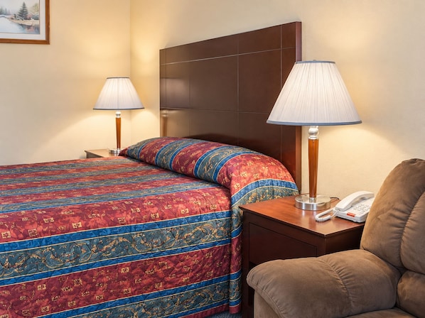 Habitación de hotel con cama, dos lámparas de noche, un teléfono y un sillón marrón.