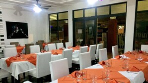 A restaurant with multiple tables set for dining, white chairs, and orange tablecloths. - Hotel Wagelia Turrialba (Turrialba)
