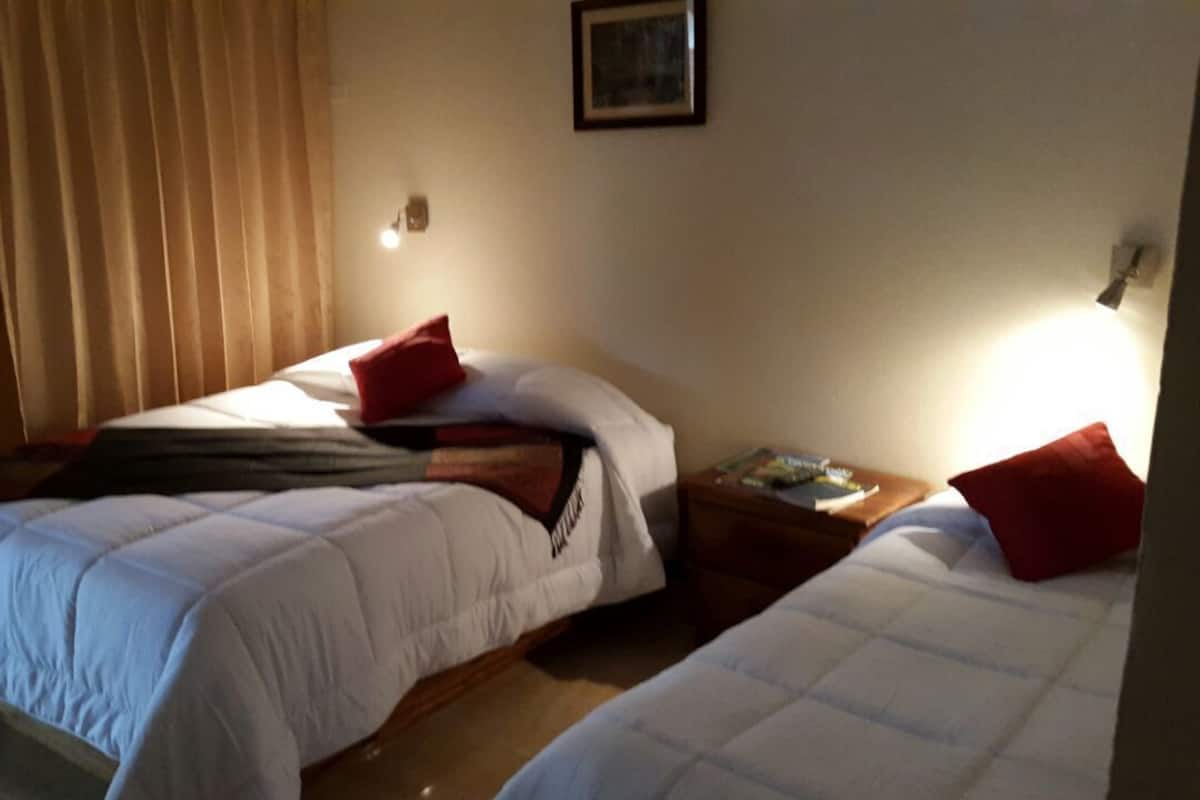 A room with two beds, each with a pillow and a nightstand.