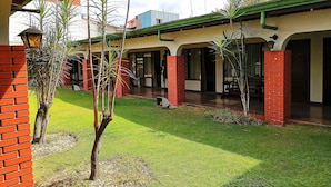 A courtyard with a green lawn, brick pillars, and a covered walkway. - Hotel Wagelia Turrialba (Turrialba)