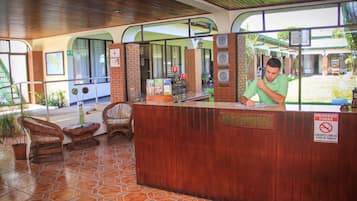 Uma área de recepção com balcão de madeira, cadeiras de vime e piso de azulejos.