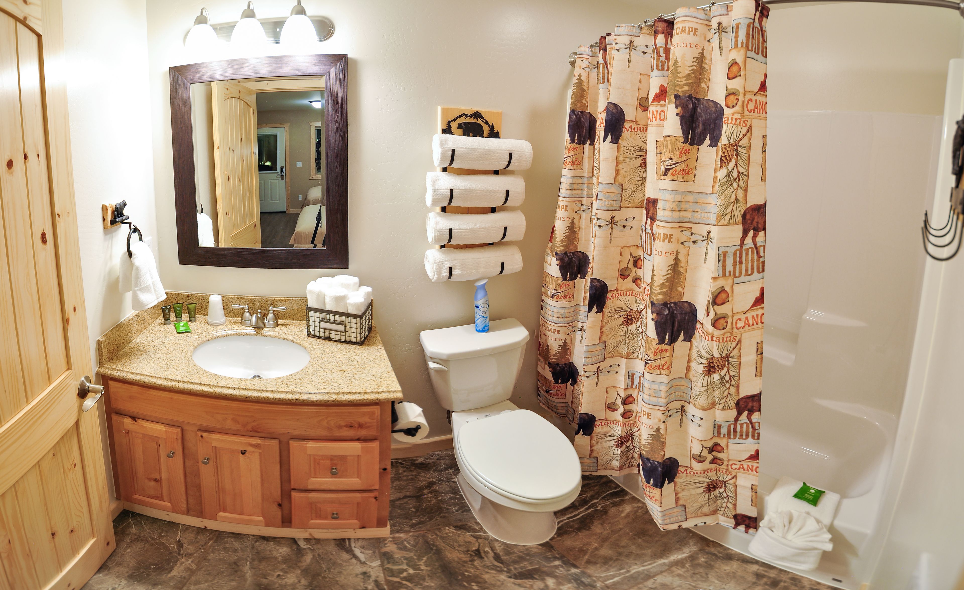 Un baño con tocador de madera, un lavabo, un inodoro y una cortina de ducha con un diseño de oso.