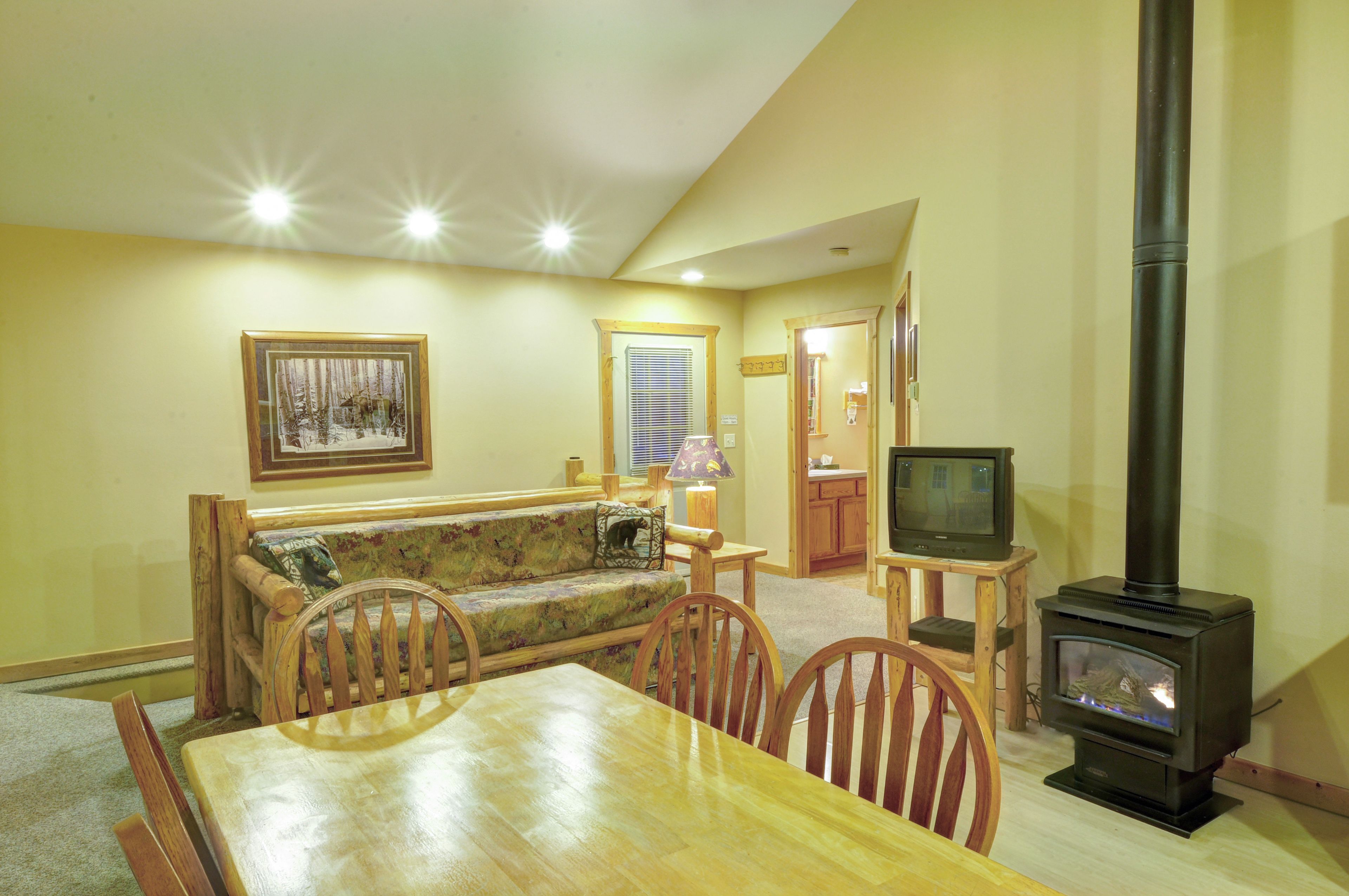 A cozy living room with a wooden dining table, chairs, a sofa, a fireplace, and a television.