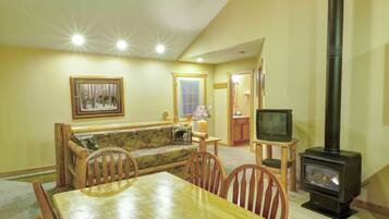 A cozy living room with a wooden dining table, chairs, a sofa, a fireplace, and a television.