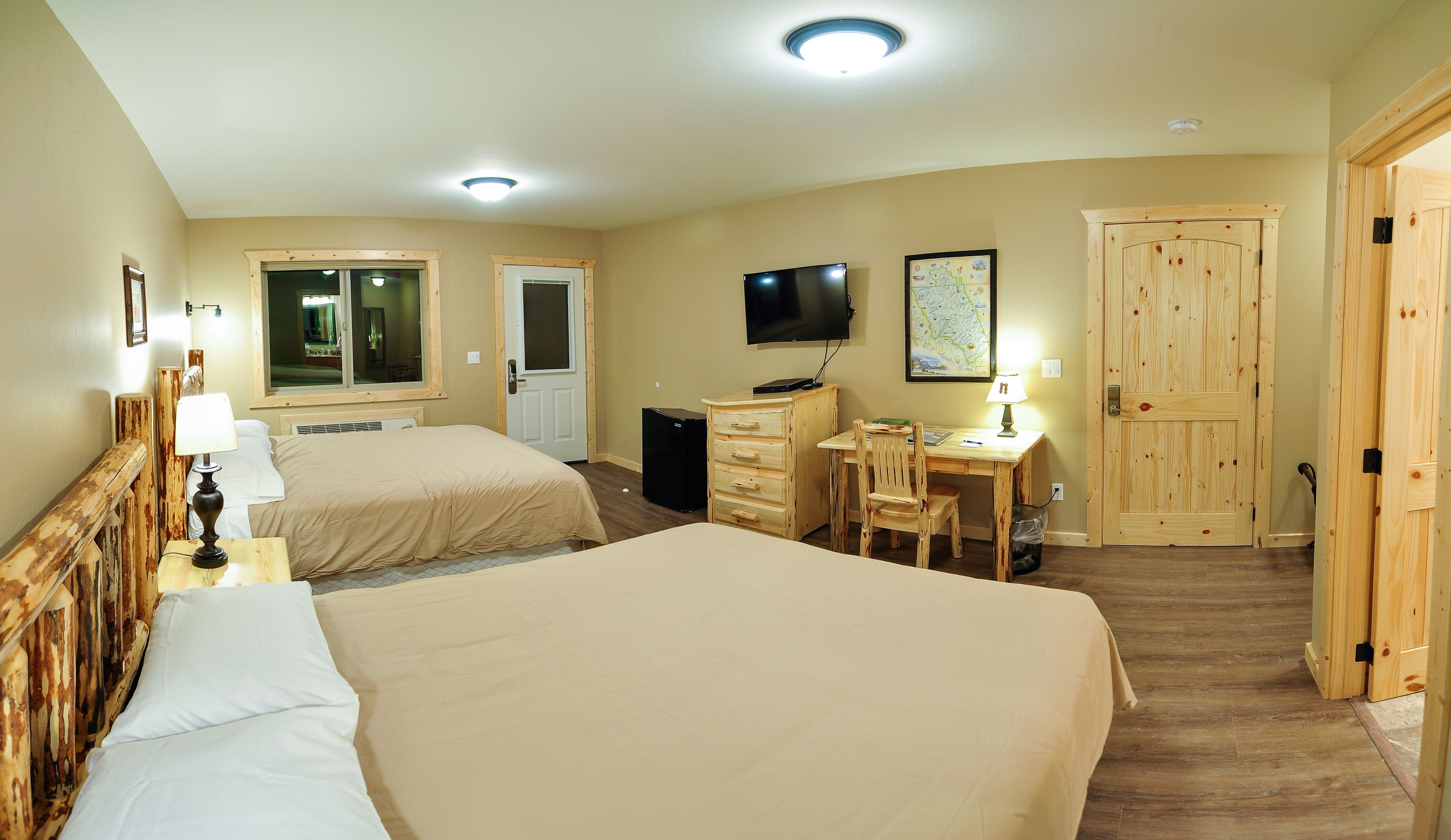 A hotel room with two beds, a desk with a chair, a television, and wooden doors.