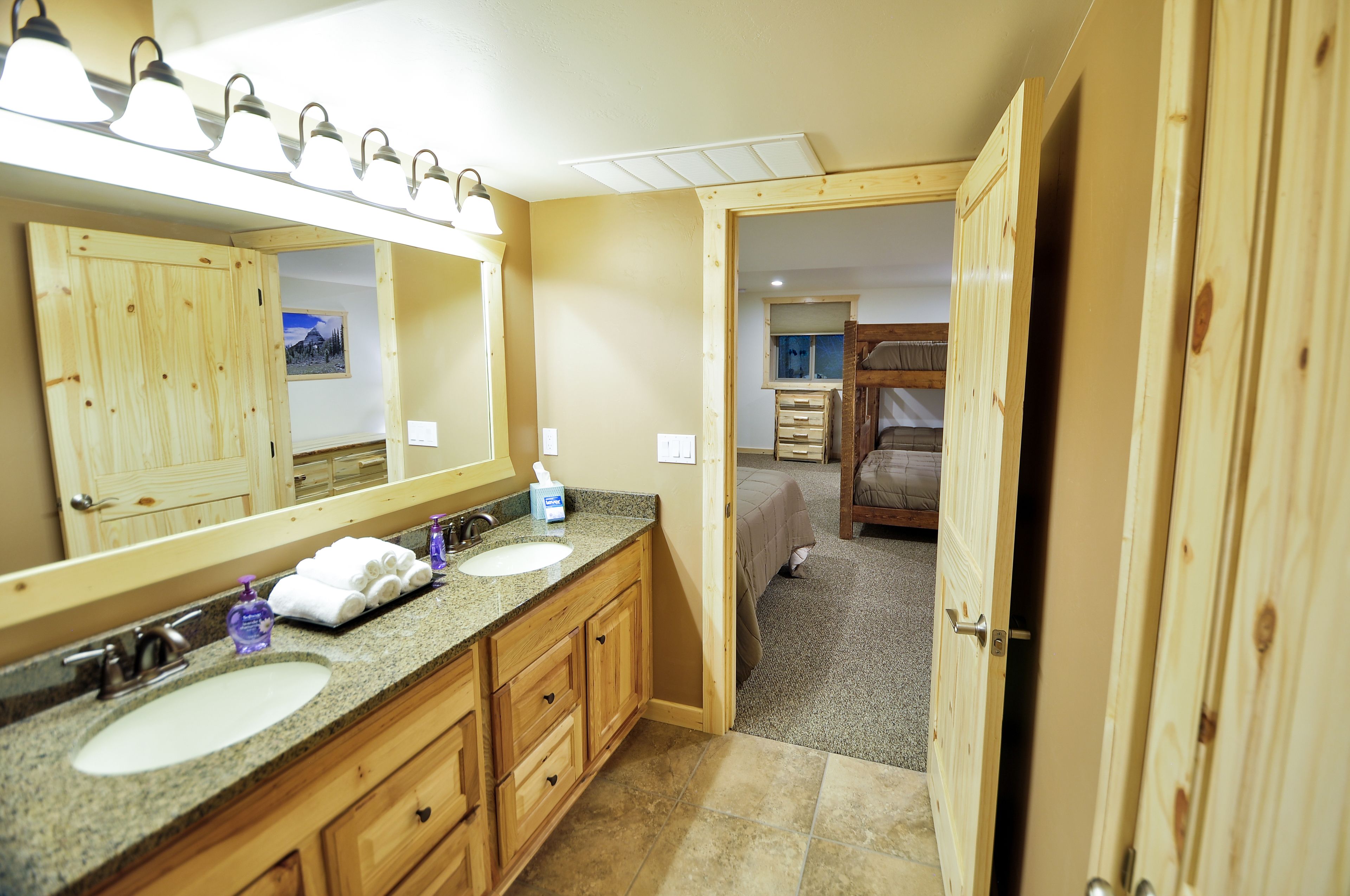 A bathroom with a large mirror, two sinks, and wooden cabinets.