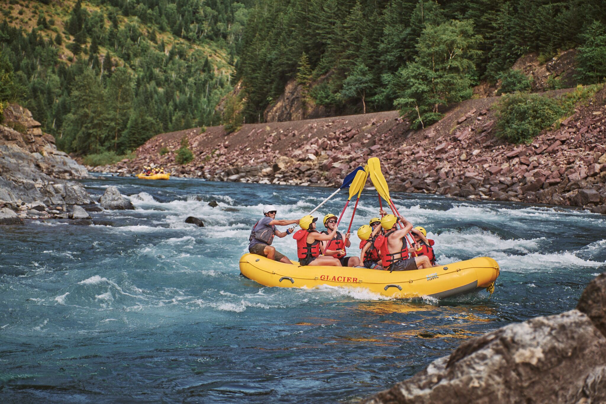 A group of people in a yellow inflatable raft on a river surrounded by rocky terrain and dense forest.