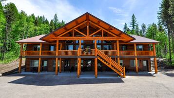 A two-story log cabin with a balcony, a staircase, and a view of the surrounding forest.