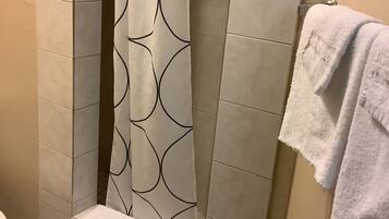 Un baño con cortina de ducha estampada con un diseño geométrico, un perchero con una toalla blanca, y paredes y suelo con azulejos.