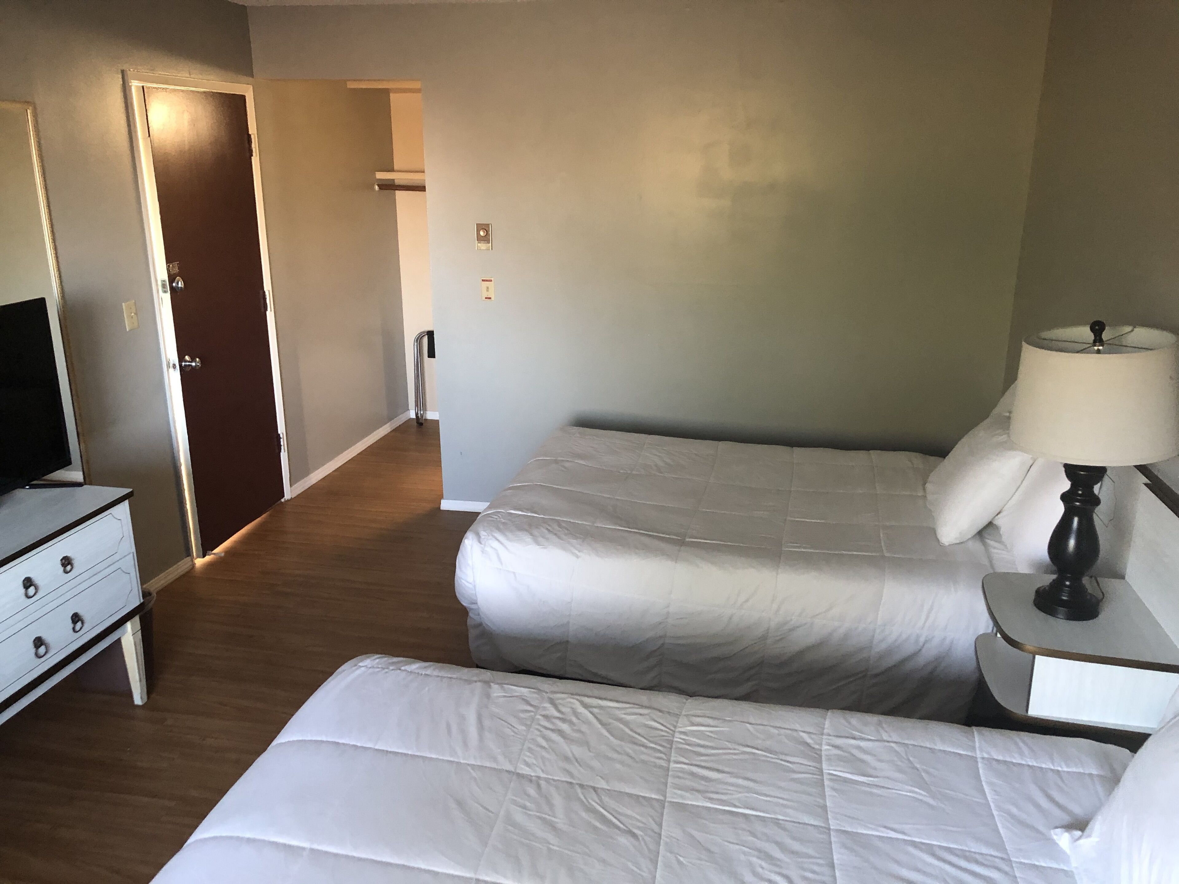 Ett hotellrum med en säng, ett nattduksbord med en lampa, en byrå och en tv.
