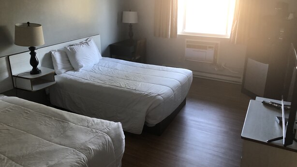 A hotel room with two beds, a nightstand with a lamp, a desk with a remote control, and a window with curtains. - Riverside Inn Dallas (Dallas)