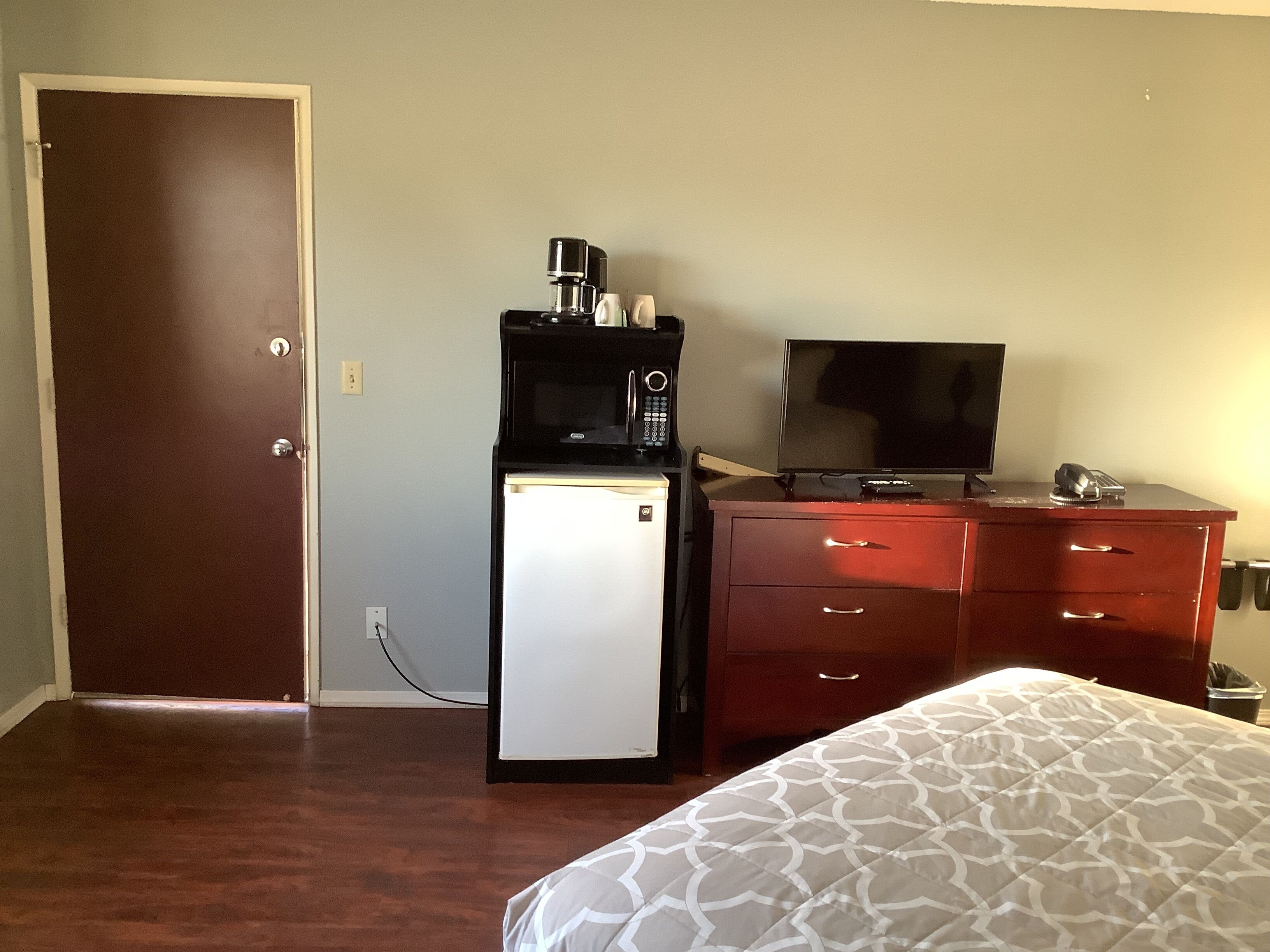 A hotel room with a bed, a desk with a computer, a refrigerator, and a television.