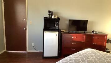 A hotel room with a bed, a desk with a computer, a refrigerator, and a television.