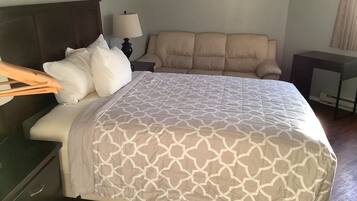 A neatly made bed with a patterned bedspread, a bedside lamp, a chair, and a small table with a lamp.