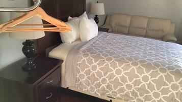 A neatly made bed with a patterned bedspread, a wooden nightstand with a lamp, and a hanging coat rack.