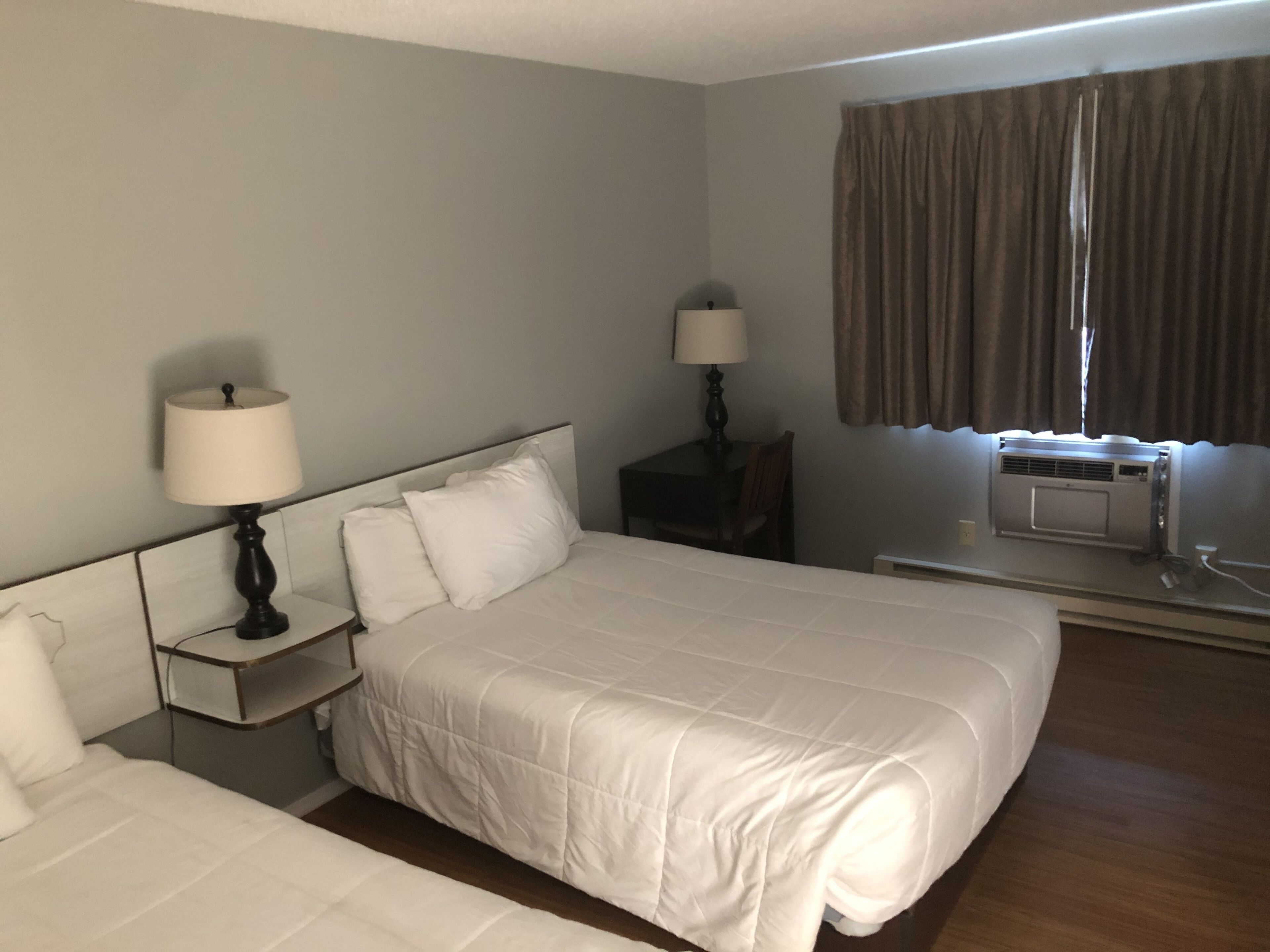 Quarto de hotel com uma cama grande, uma mesa de cabeceira com abajur, uma mesinha com abajur e um aparelho de ar condicionado.