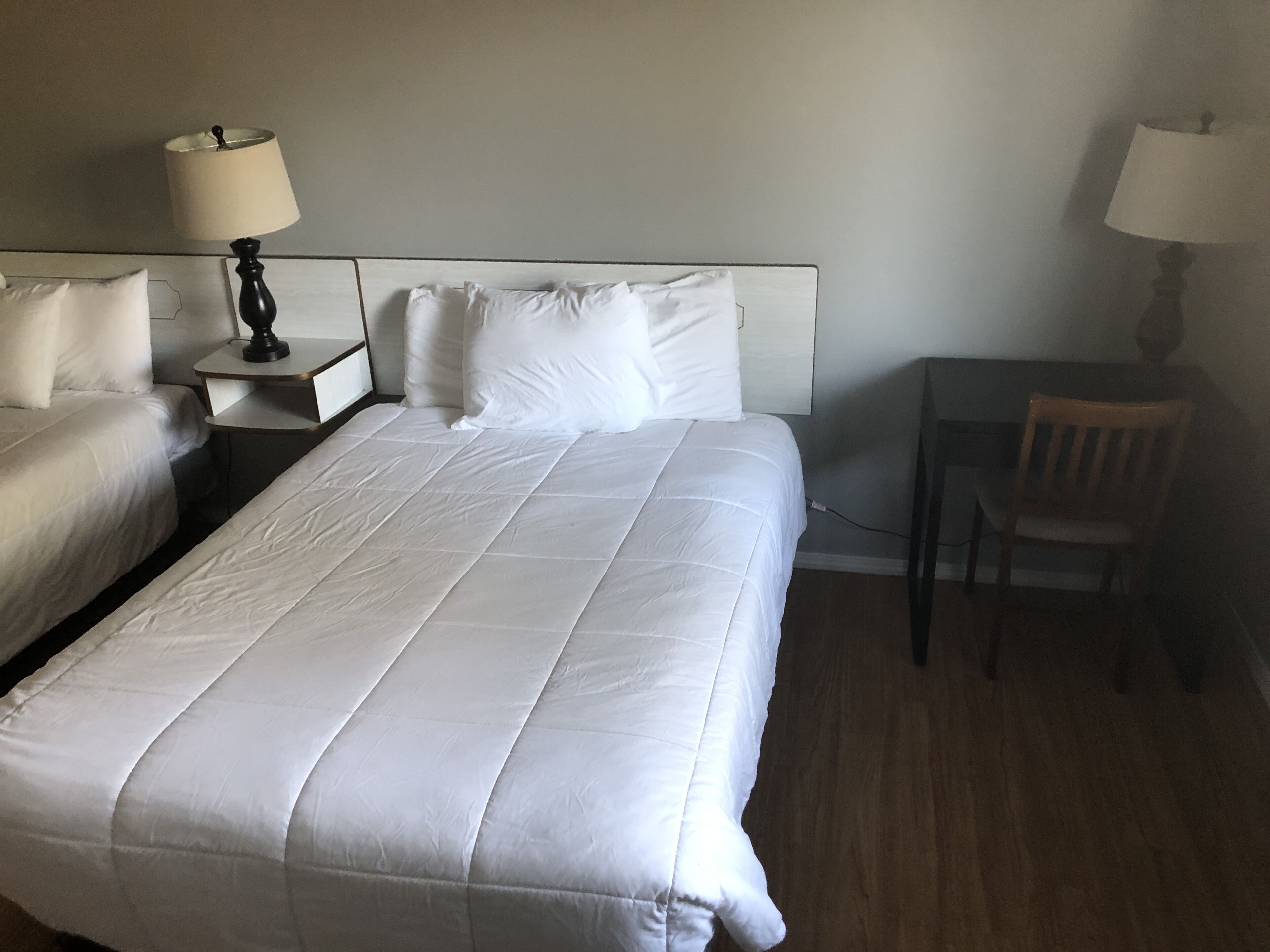 A hotel room with a large bed, two bedside tables with lamps, a chair, and a desk.