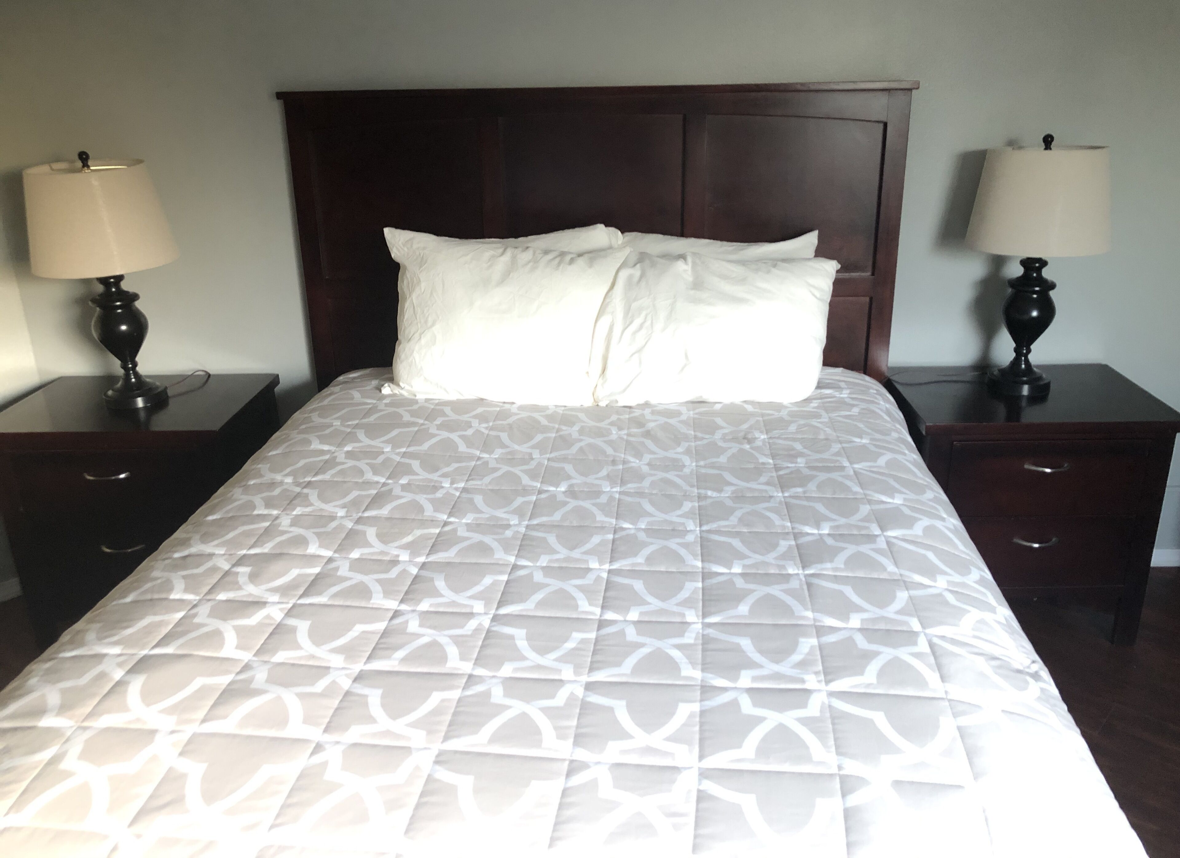 A neatly made bed with a patterned bedspread and two bedside tables with lamps.