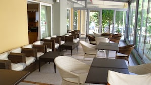 A hotel lobby with wicker furniture, a seating area, and large windows offering a view of the outdoors. - Hotel Cybele (Lykovrysi-Pefki)