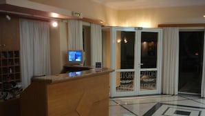 A hotel reception area with a wooden reception desk, a digital screen, and a glass door leading to a balcony. - Hotel Cybele (Lykovrysi-Pefki)