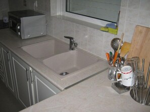 A kitchen with a sink, a microwave, and various utensils in a holder. - Hotel Cybele (Lykovrysi-Pefki)