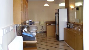 A compact kitchen with a refrigerator, a coffee maker, and a sink. There are wooden cabinets and a bar stool. - Hotel Cybele (Lykovrysi-Pefki)
