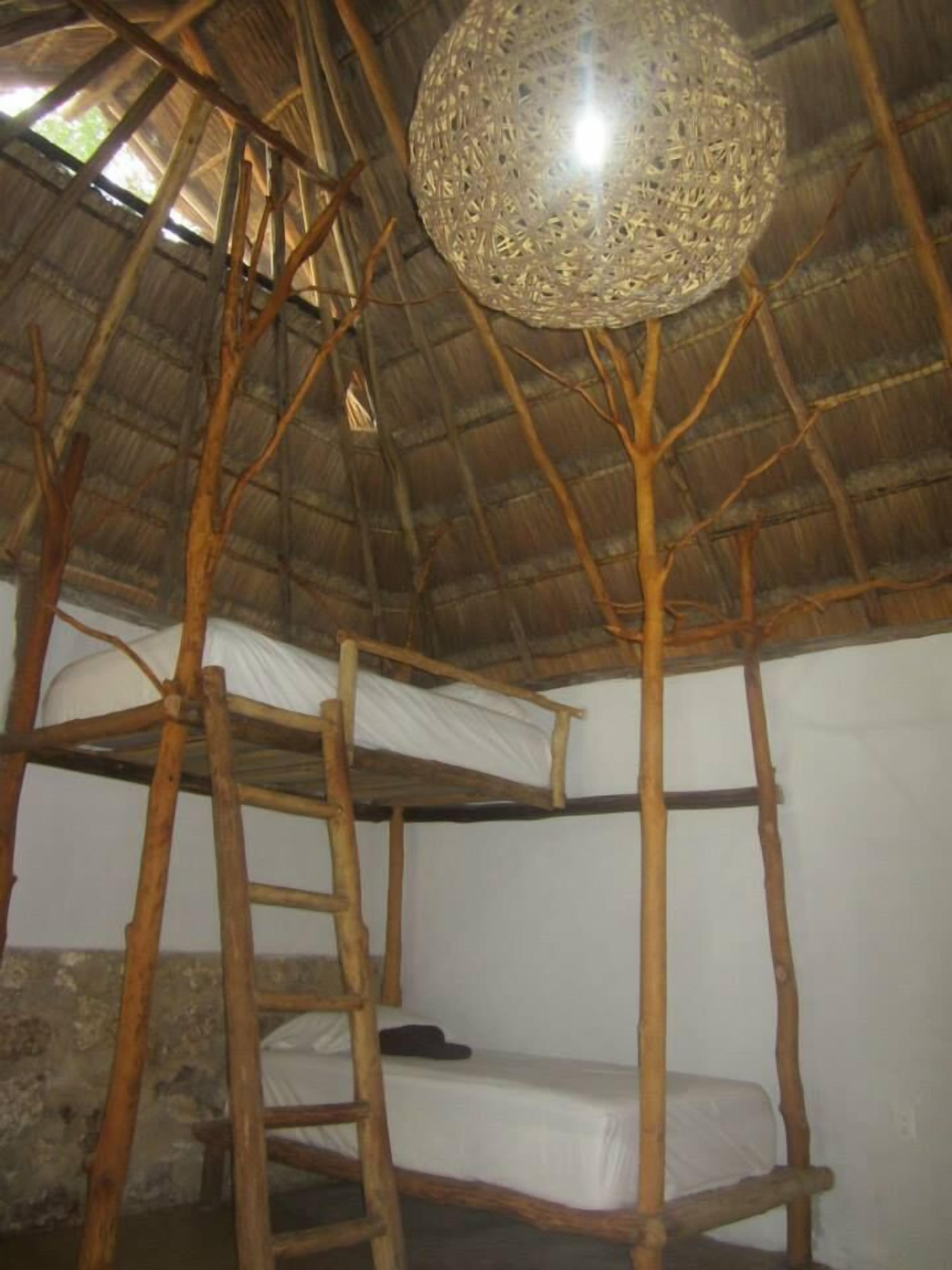 A rustic room with a thatched roof, wooden bunk beds, and a woven light fixture.