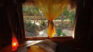 A room with a bed, a window with a view of a garden, and a hanging yellow cloth.