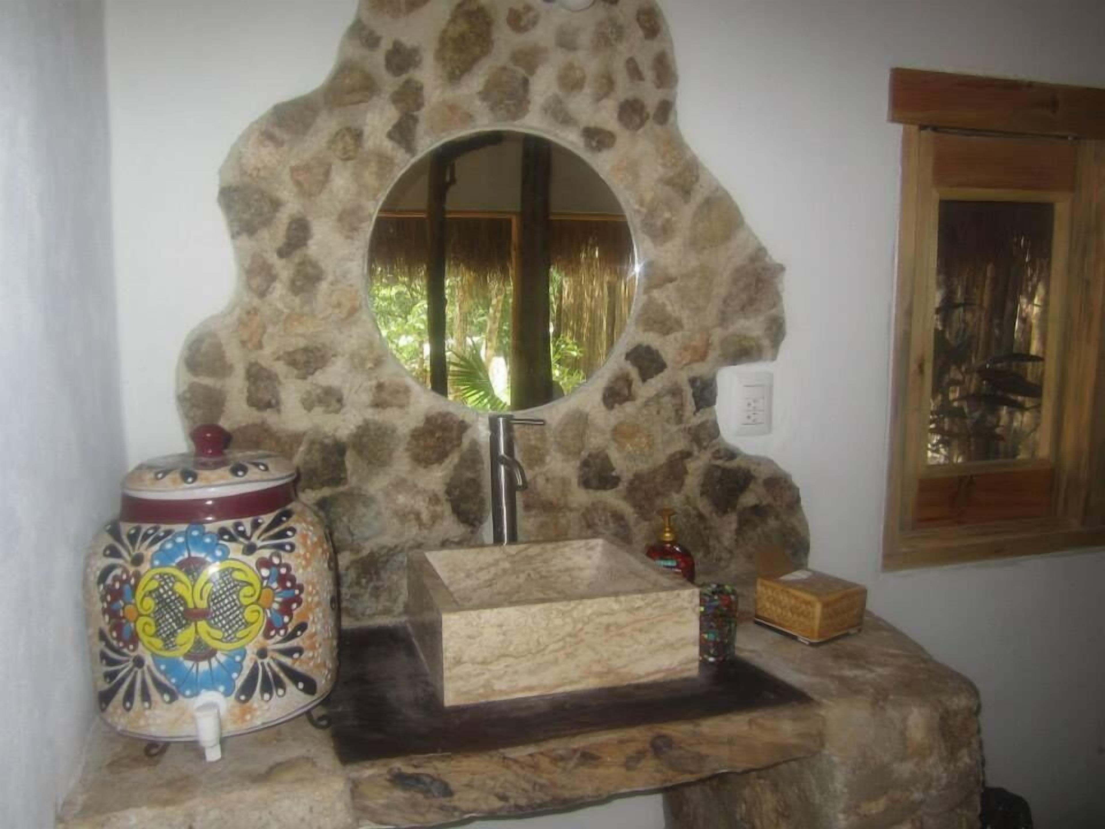 A bathroom with a stone sink, a mirror, and a decorative vase.