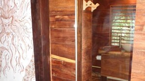 A wooden interior with a stone floor, a wooden-framed mirror, and a bathroom visible through the mirror.
