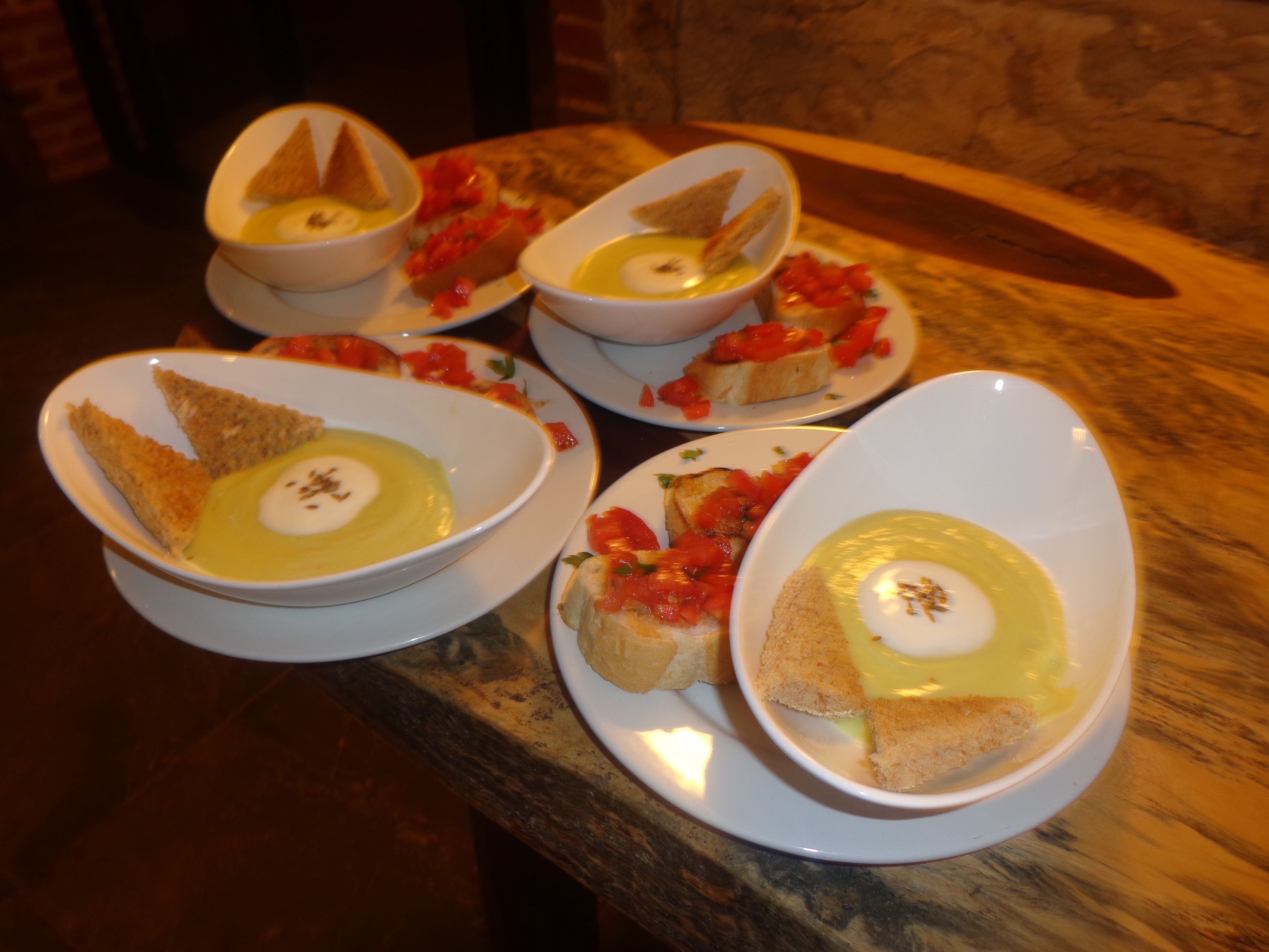 Een tafel met vier kommen soep en brood, elk met een toefje room en een beetje kruiden.