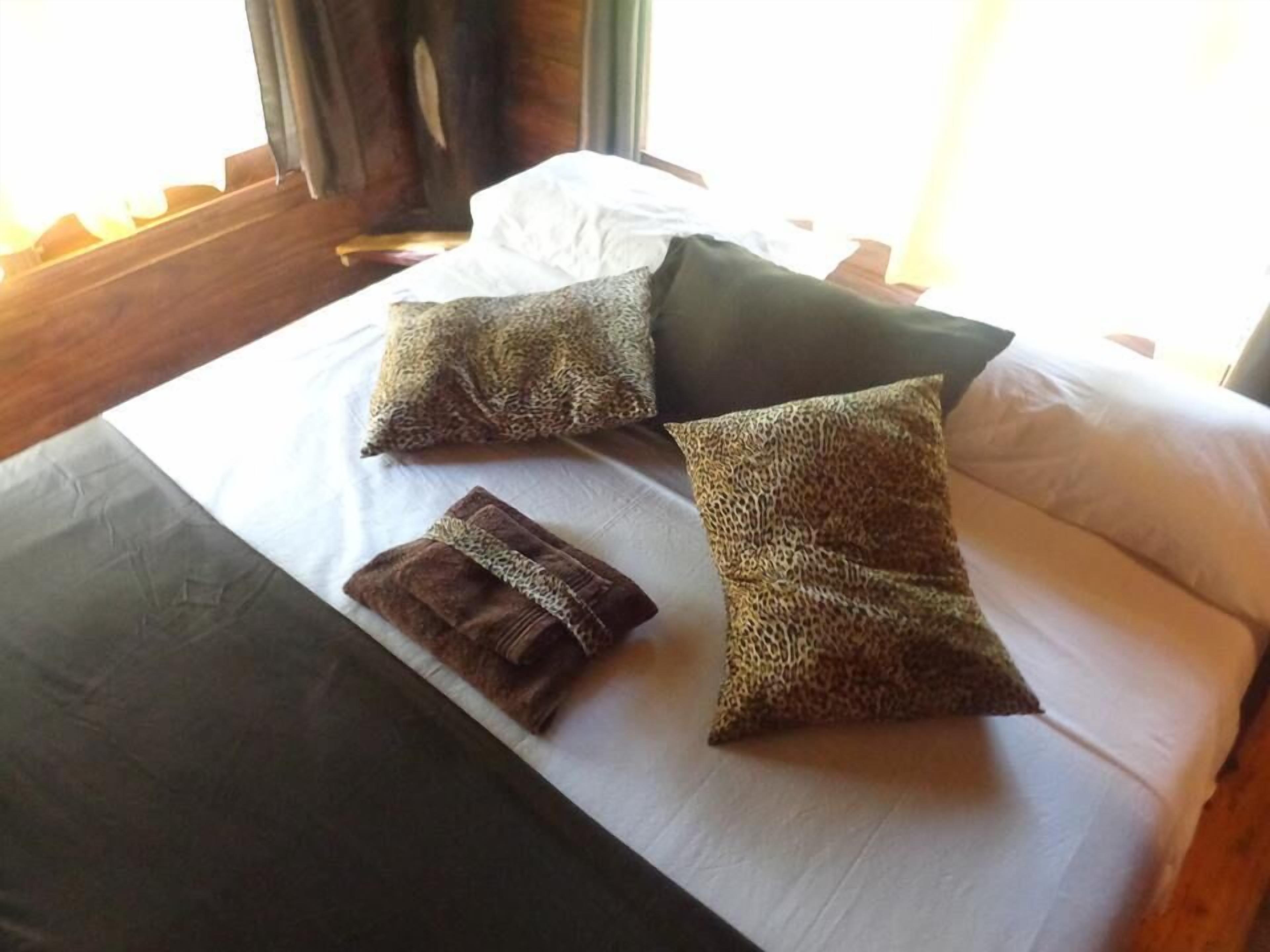 Una cama con sábana blanca, dos almohadas de estampado de leopardo, una toalla marrón oscuro y una manta marrón oscuro.