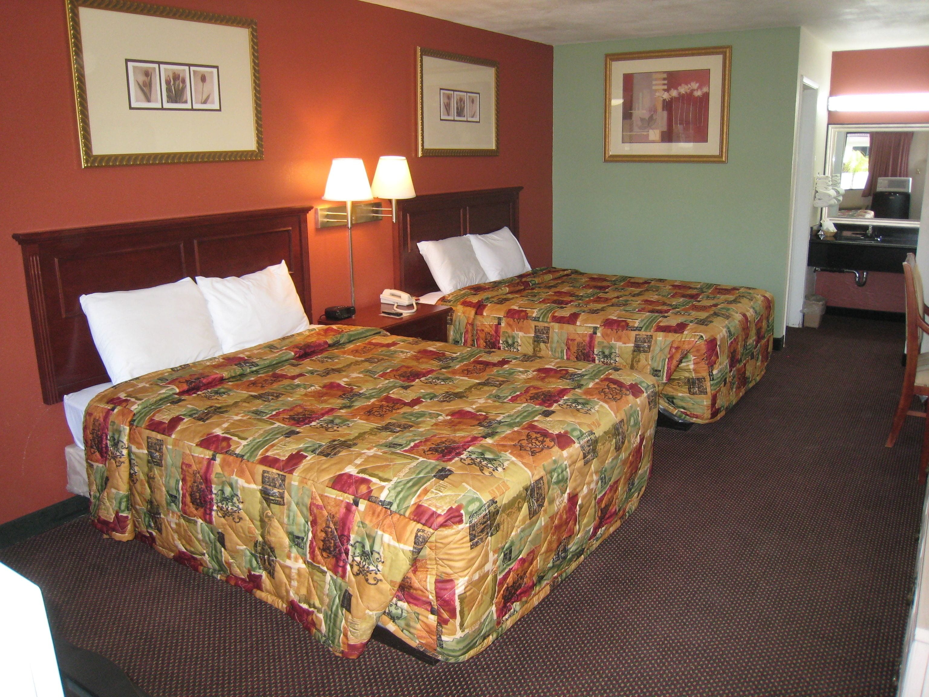 A hotel room with two beds, a desk, and a bathroom.