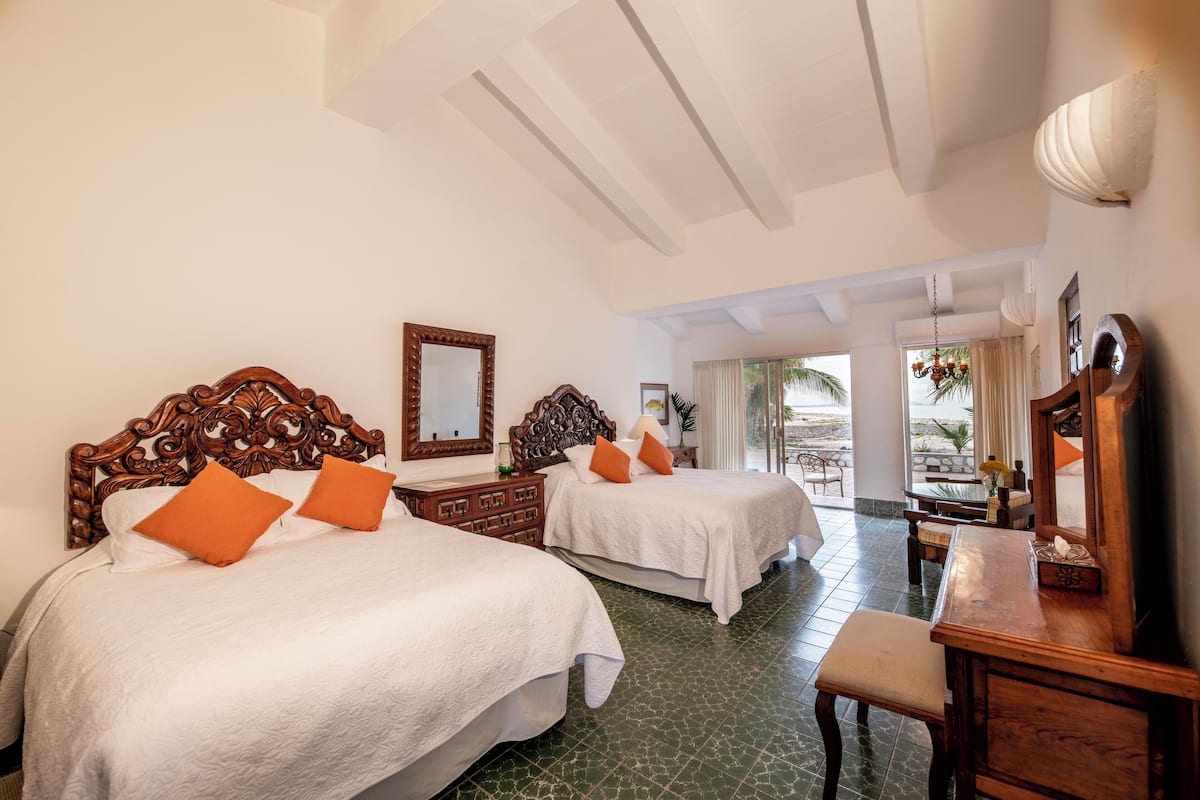 A hotel room with two beds, wooden headboards, a wooden dresser, and a large mirror.