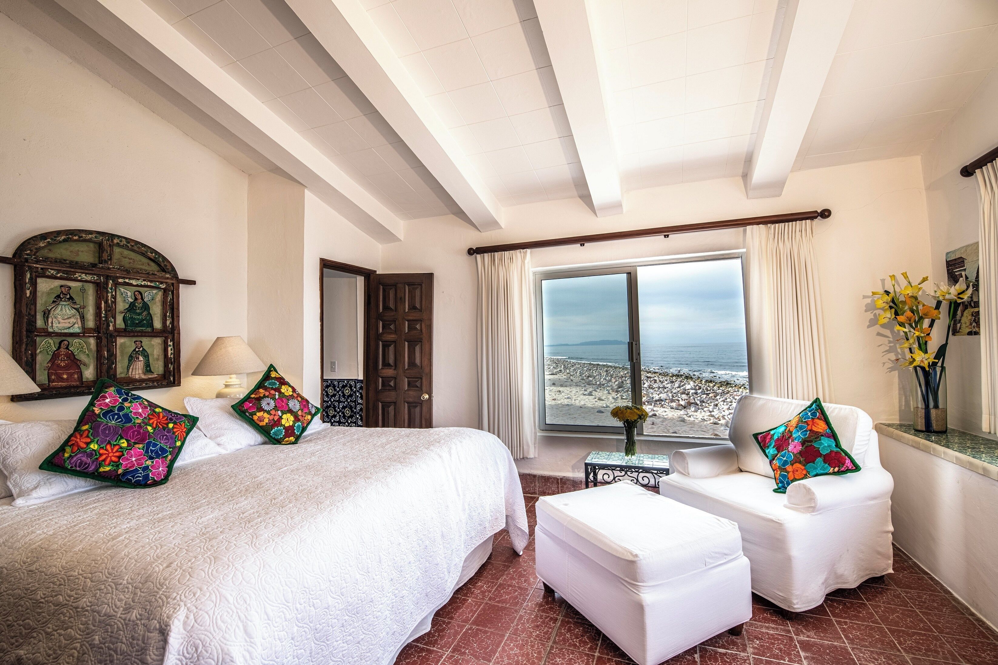 A hotel room with a large bed, two chairs, a small table, and a view of the beach.