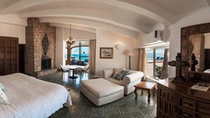 A spacious bedroom with a large bed, a sitting area with a view of the sea, and a stone fireplace. - Rancho Las Cruces Baja California Sur (Las Cruces)
