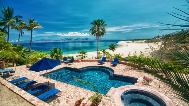 A pool area with lounge chairs and umbrellas, a clear view of the ocean, and a mountainous backdrop. - Rancho Las Cruces Baja California Sur (Las Cruces)