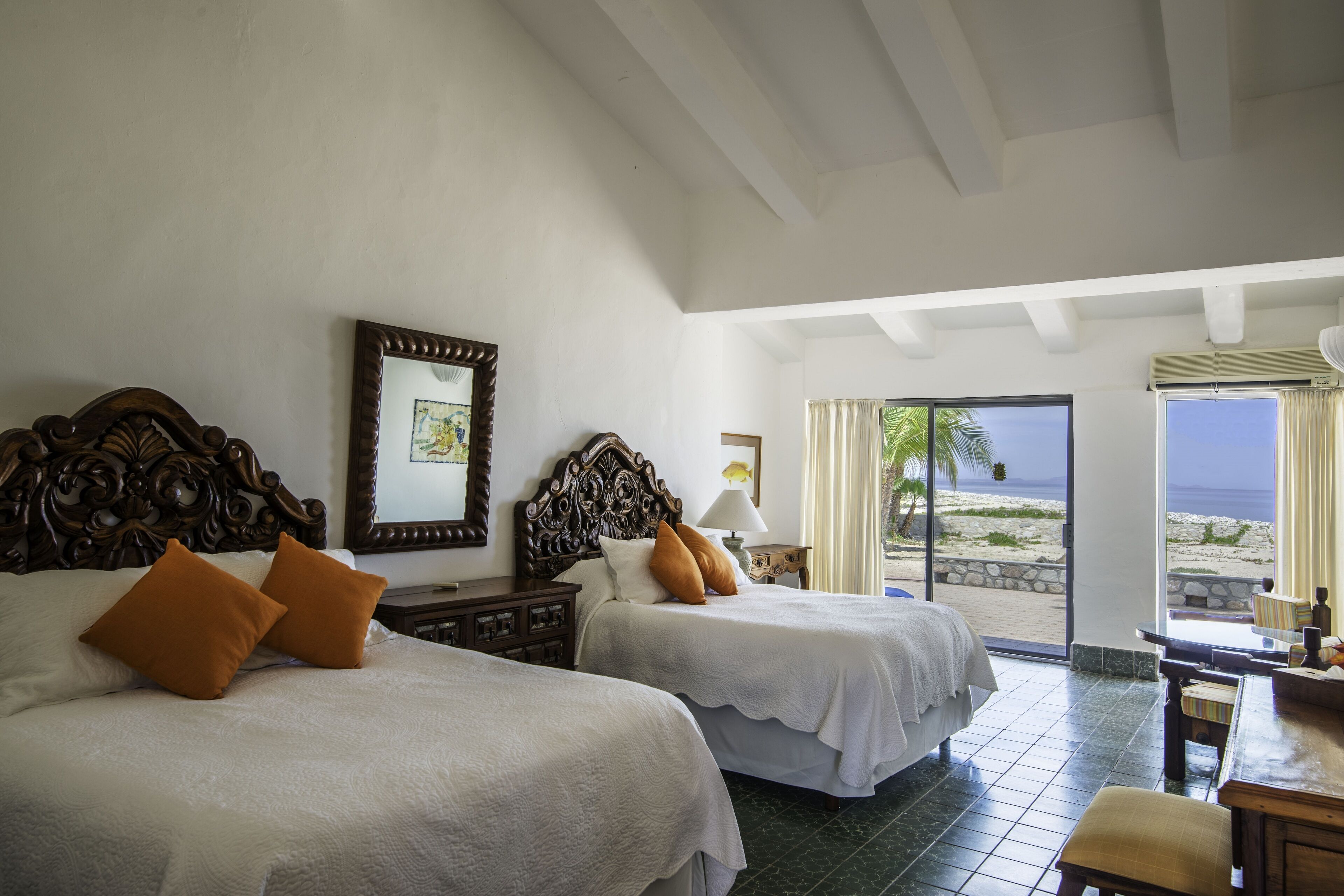 A hotel room with two beds, a desk, and a view of the beach.