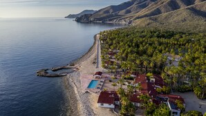 An aerial view of a coastal resort with a swimming pool, palm trees, and a beach. - Rancho Las Cruces Baja California Sur (Las Cruces)
