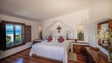 A bedroom with a large bed, a view of the sea through a window, and a decorative wall with a cross.