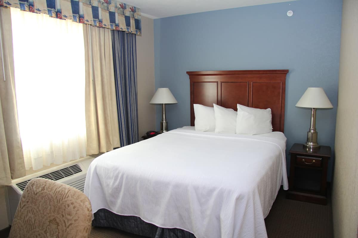 A hotel room with a large bed, two bedside lamps, a nightstand, and a window with curtains.