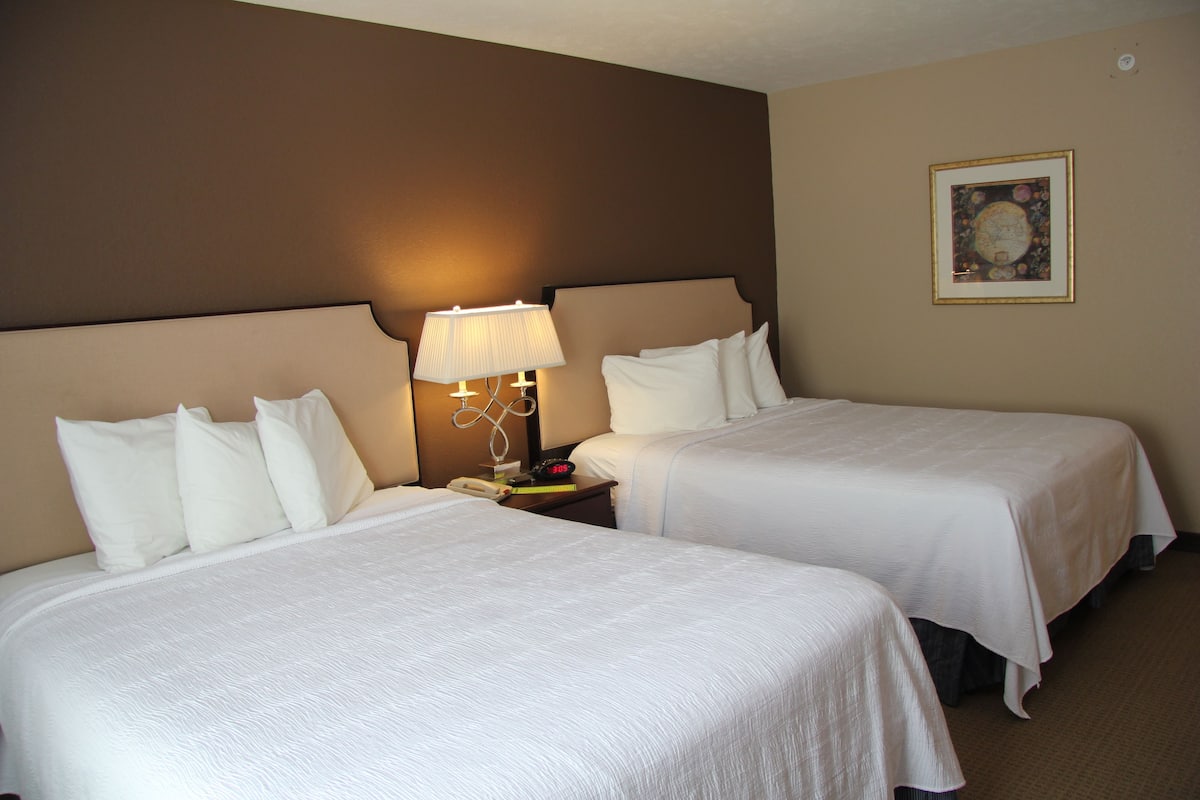 A hotel room with two beds, a nightstand with a lamp, and a framed picture on the wall.